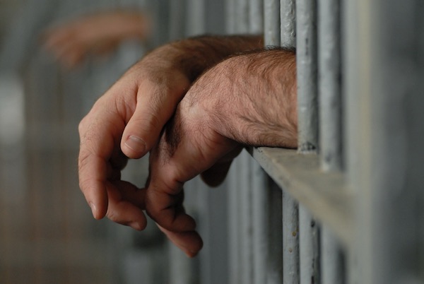 A prison inmate drapes their hands over their cell bars.