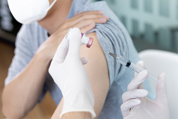 A doctor uses a small syringe to draw up COVID-19 vaccine solution in preparation for injection.