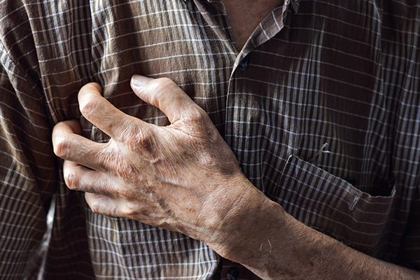 Image depicts an older person clutching a hand over their chest, which illustrates some of the heart-related side effects of immunotherapy drugs.